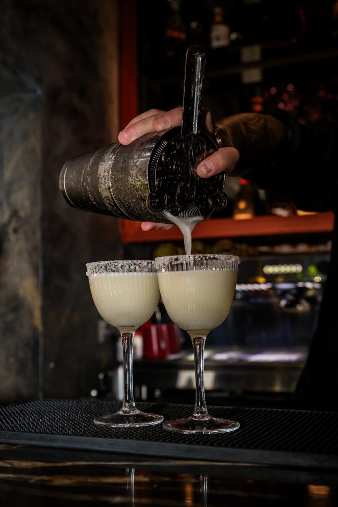 Bartender straining a cocktail into two coupe glasses