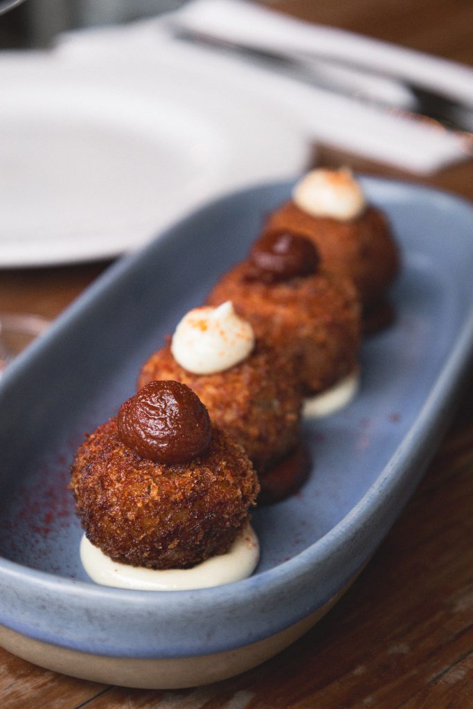 Row of croquettes topped with aioli on a blue ceramic dish