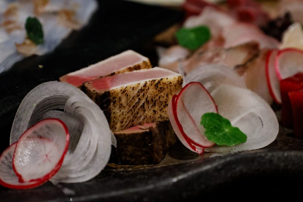 Seared tuna with thinly sliced radish and fresh herbs on a dark plate