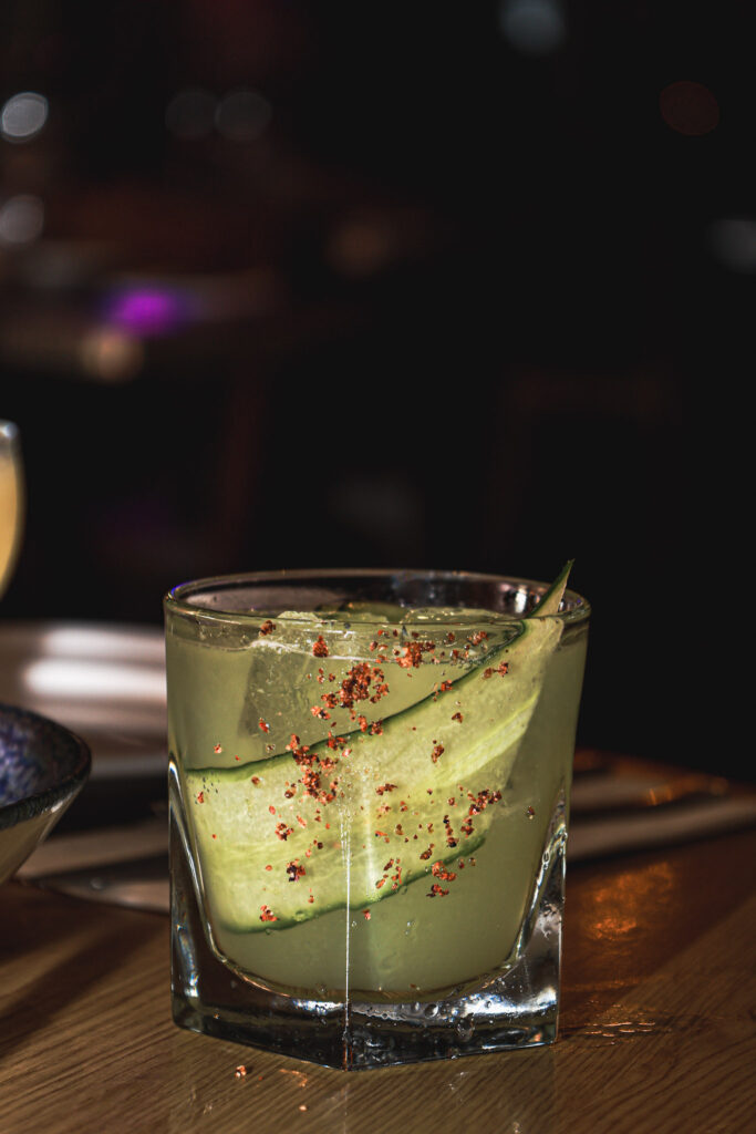 Cucumber cocktail with a spiced rim in a moody bar