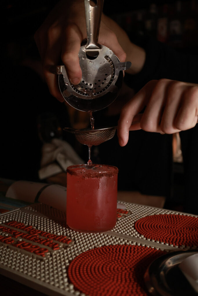 Bartender pouring a cocktail into a glass at the bar