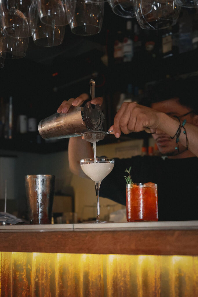 Bartender straining a cocktail into a coupe glass at the bar