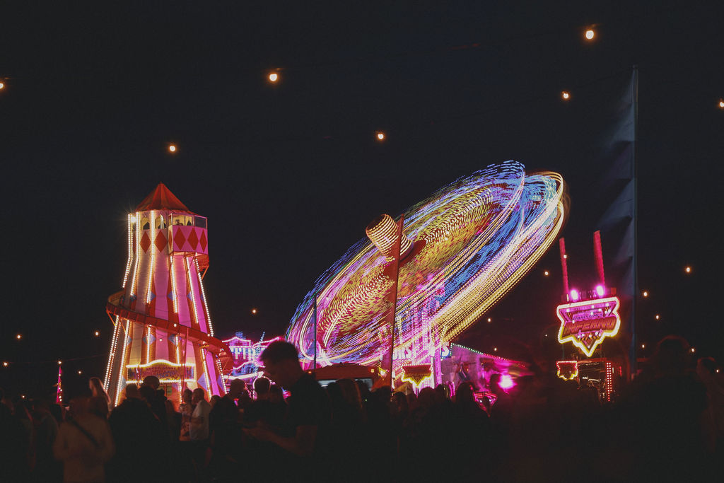 Fairground rides lit up at night above a crowd in silhouette