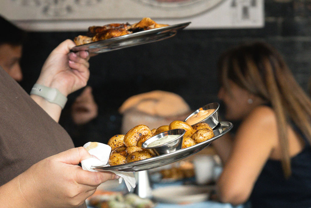 Server carrying plates of roast potatoes and chicken through the dining room